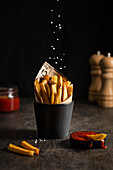 French fries being sprinkled with salt and served with ketchup