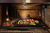 A flaming charcoal grill, with a selection of meat and vegetables