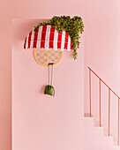 Red and white striped awning on round window against pink wall