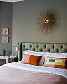 Vintage sunburst mirror above buttoned green headboard