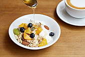 Granola, yoghurt and fresh fruit with honey being poured