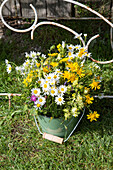 Colorful bouquet of wild flowers in green bucket on lawn