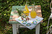 Two bottles with orange drink, wild flowers and tablecloth on wooden stool