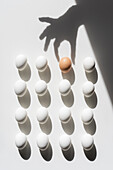 Weiße Eier und ein braunes Ei, darüber Schatten einer Hand