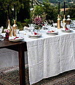 Festlich gedeckter Tisch im Garten mit Blumenstrauß und goldenen Kerzenhaltern