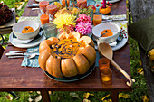 Autumnal garden table with pumpkin soup in a pumpkin and floral decorations