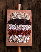 Various beans arranged in rows on a wooden cutting board