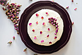 Rose cake decorated with dried rose buds and petals on a purple plate