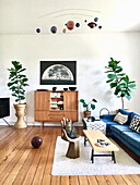 Blaues Polstersofa, Couchtisch, Stuhl in Handform, Retro Highboard, und Zimmerpflanzen im Wohnzimmer