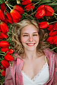 Junge blonde Frau umgeben von roten Tulpen liegt auf einer Wiese