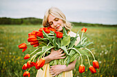 Junge blonde Frau mit rotem Tulpenstrauß auf einer Wiese