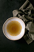 Clear homemade chicken or duck broth bouillon in ceramic bowl on black wooden table table.