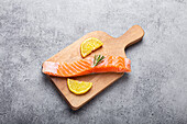 Raw salmon fish fillet with lemon wedges and rosemary on wooden cutting board