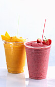 Strawberry smoothie and mango smoothie in plastic cups