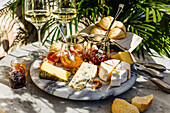 Käseplatte mit Weichkäse, Fruchtsaucen und Weißwein auf Tisch im Freien