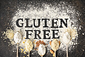 'Gluten free' Schriftzug in Mehl auf Vintage-Backblech und Löffel mit verschiedenen glutenfreien Mehlsorten