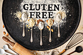 Gluten free written in flour on vintage baking sheet, kitchen utensils and spoons of various gluten free flour