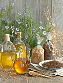 Three bottles of linseed oil and golden and brown linseed oil seeds, linseed flowers and dried linseed capsules