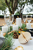 Table with dinnerware and cutlery near decorative fir branches and candles with walnuts and cinnamon sticks on plates