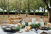 Table setting decorated with candles and cones placed near wooden chairs for Christmas dinner in nature