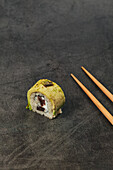 Sushi-Röllchen mit Reis, Avocado und Frischkäse daneben Essstäbchen