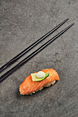 Nigiri sushi with slice of salmon on rice topped with thin slice of avocado and cream cheese served near chopsticks