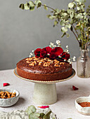 Biscuit chocolate cake garnished with flower buds and nuts served on stand on table