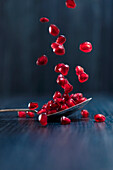 Red fresh juicy pomegranate fruits seeds falling on spoon and dark wooden surface on blue background