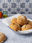 Freshly baked bread buns heaped on baking paper on plate and served on kitchen table