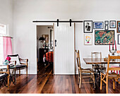 Dining table with sewing machine frame and picture gallery in dining room, view through open sliding door into bedroom