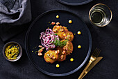 Mini-Lachspuffer mit Zwiebelsalat auf schwarzen Teller, mit goldenem Besteck