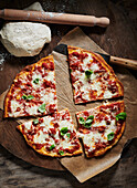 Pizza Margherita auf Pizzabrett daneben Pizzateig und Teigroller