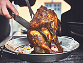Slicing Tandoori chicken onto a vertical poultry roasting tray