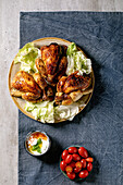 Whole grilled roasted mini chicken with green salad on ceramic plate, yogurt sauce, cherry tomatoes