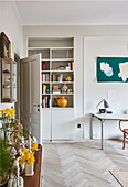 A built-in shelf in a living room with a herringbone parquet floor and a desk