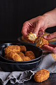 Crop unrecognizable person demonstrating half of yummy deep fried croquette with cheese filling on black background