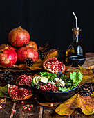 Pomegranate salad in bowl severed on wooden table with autumn leaves and bottle of olive oil on black background