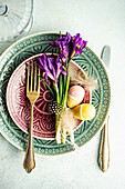 Ostergedeck mit Keramiktellern, Iris, Eiern und Federn auf Betontisch