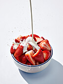 Cream being poured over strawberries in a bowl