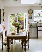 A traditional dining area to one side of a kitchen with a table and chairs vase of flowers clock mounted above a stainless steel dishwasher