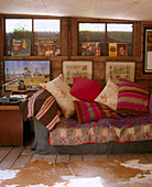 Detail einer Wand mit gerahmten Bildern und Schallplatten über einem traditionellen Sofa mit einer Vielzahl von Kissen vor einem Teppich