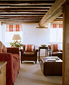 A traditional country living room with exposed wooden beams above a leather coffee table in front of a red sofa