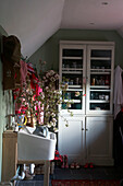 Twig arrangement in butlers sink of cloakroom with glass fronted storage unit in Rye, Sussex