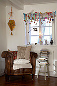 Armchair and stool with pile of books by window with Christmas decorations