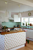 Pendant lights hang over wallpapered kitchen island