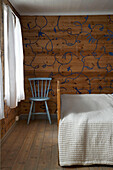 Einfacher blauer Stuhl neben dem Doppelbett in einem Schlafzimmer im Landhausstil