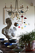 Bust and bowls with houseplant on table under chandelier light fitting