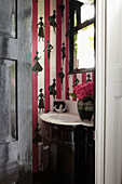 Marmorwaschbecken und Figuren auf rosa gestreifter Tapete in der Gästetoilette eines Londoner Hauses
