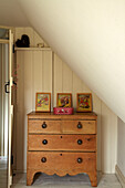 Wooden chest of drawers below slanted ceiling in Norfolk beach house, UK
