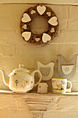 Wandkranz mit Herzen über Regal mit Teekanne, Teetasse und Dekohühnern im Haus in West Sussex, England, UK